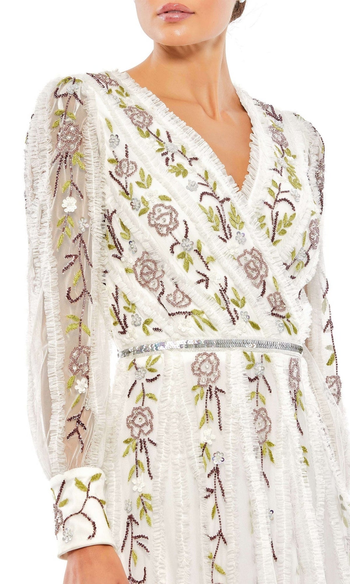 A woman in the Mac Duggal Knee Length Wedding Guest Dress 9133, a white semi-formal a-line midi dress with pink and green floral embroidery, long sleeves, V-neckline, and an elegant silver waistband.